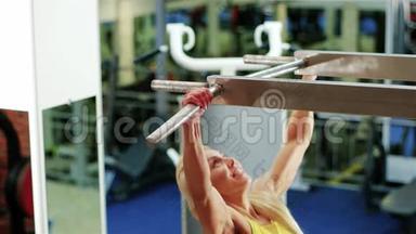 女孩做一个拉力运动，在水平杆上做运动，运动的女人在健身房里做运动
